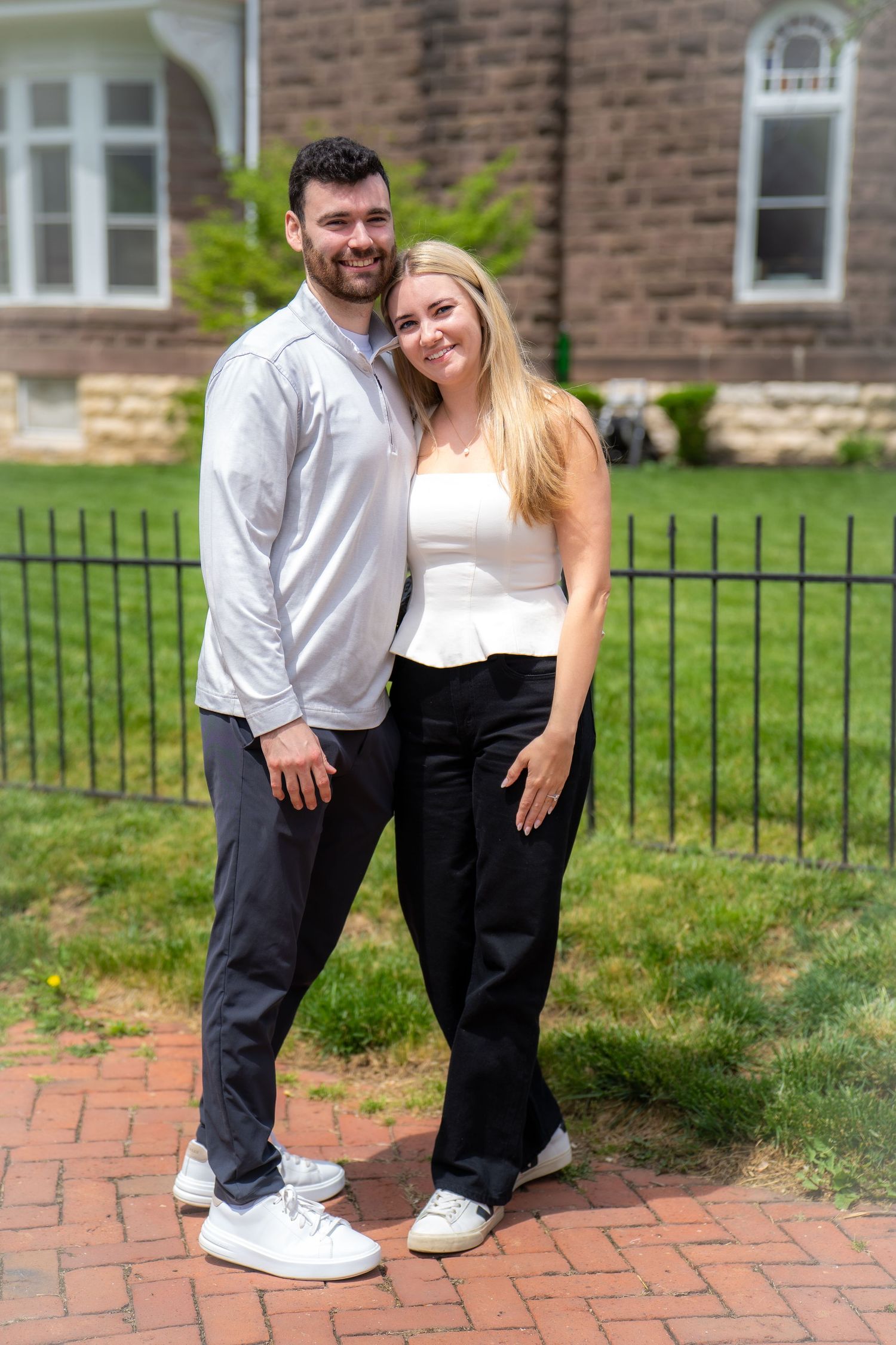Happy engaged couple smiling together outdoors near iron fence and brick building.
