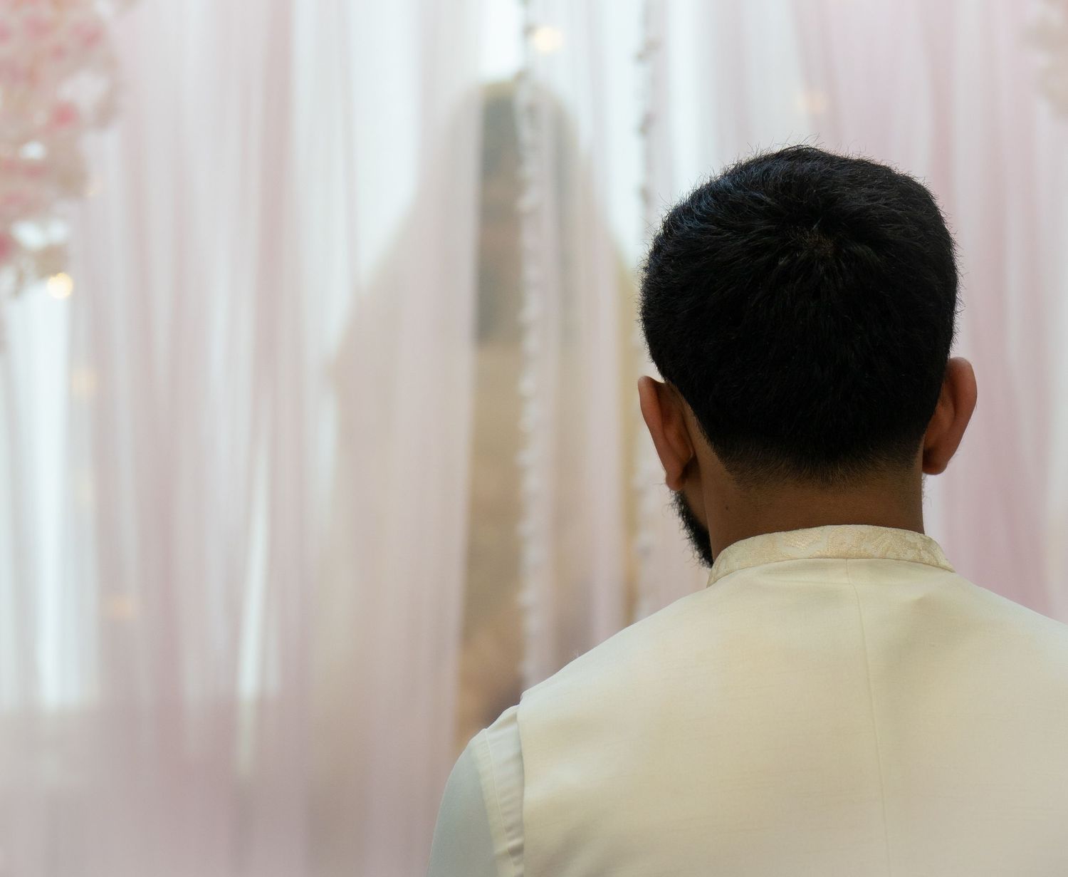 Groom in white attire viewed from behind at a wedding ceremony.
