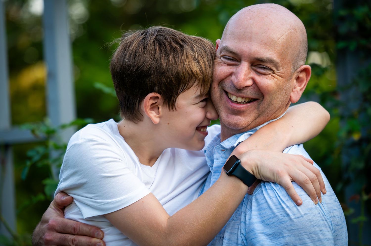 Father and son laughing and hugging each other in a joyful outdoor portrait.