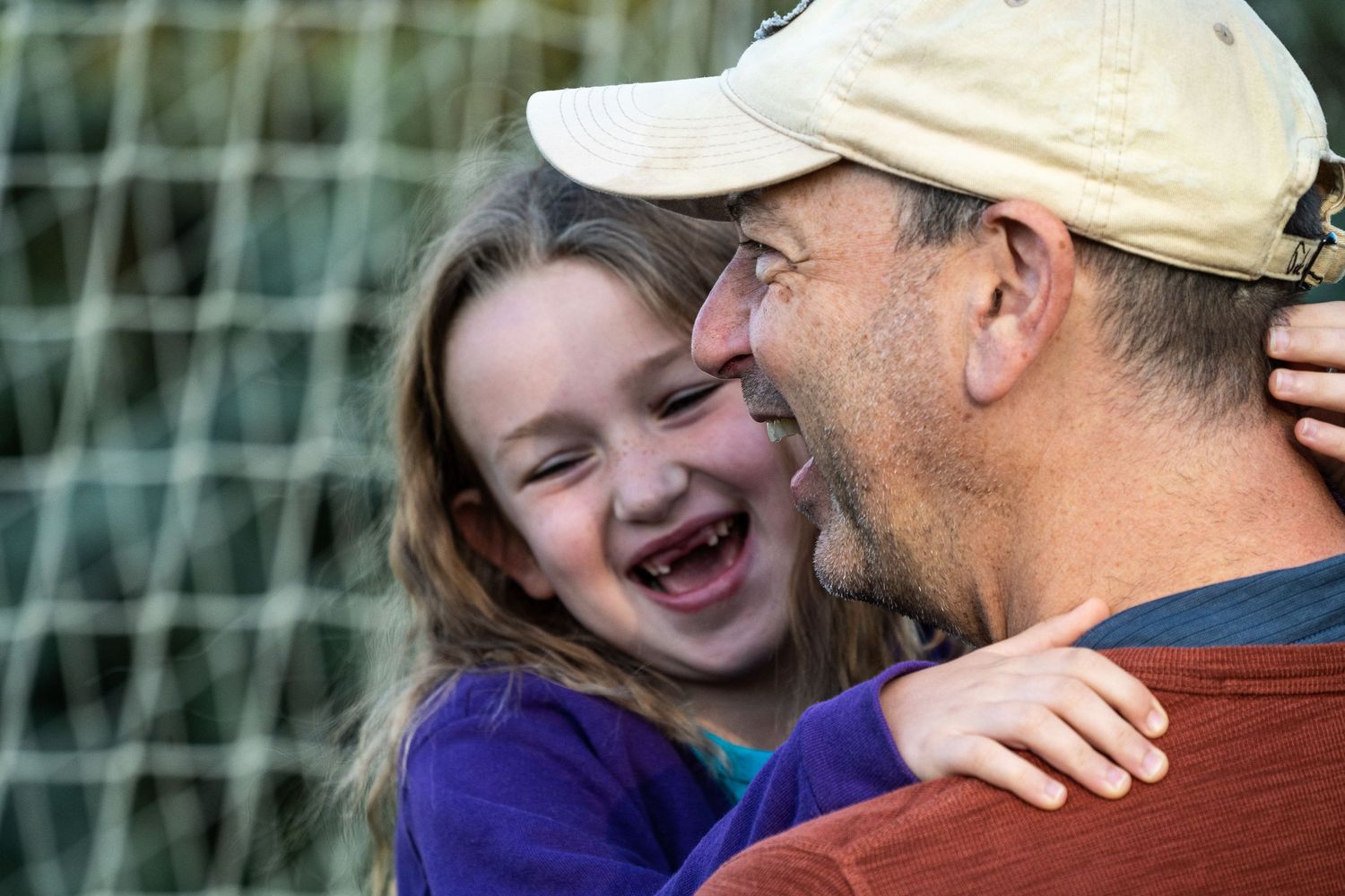 Young girl laughing joyfully while being held by a smiling man outdoors.