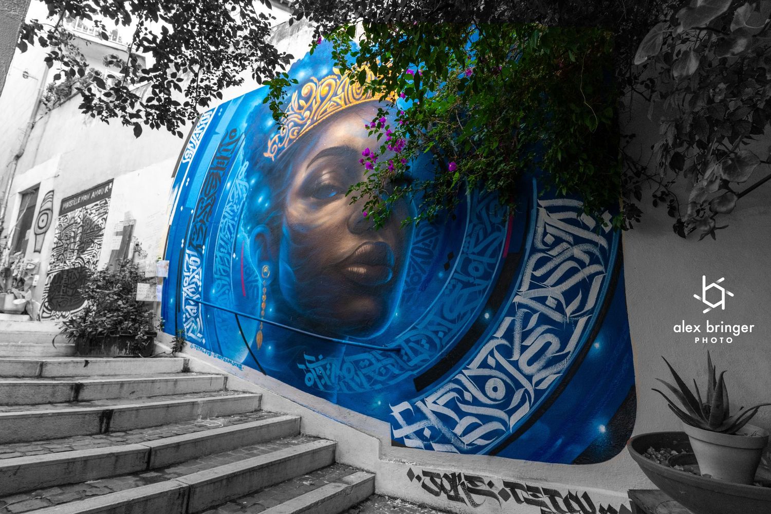 Vibrant blue street mural of a crowned woman on a building staircase in selective color photo.