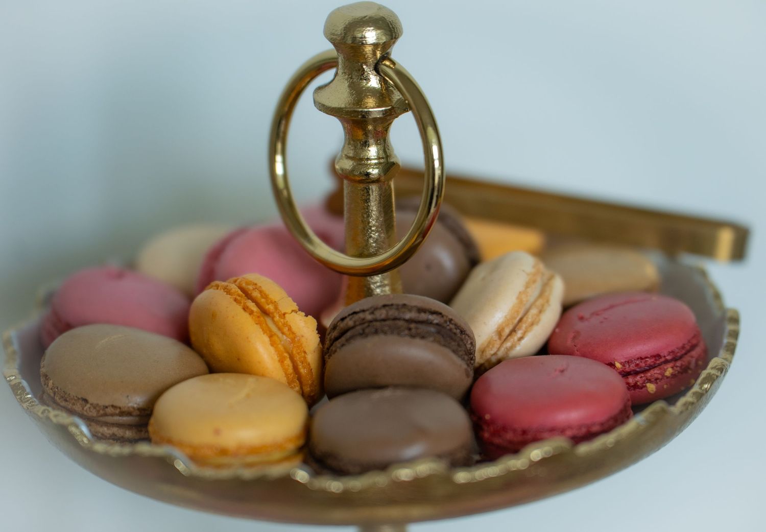 Assorted colorful French macarons arranged on a decorative gold serving dish with ornate handle.
