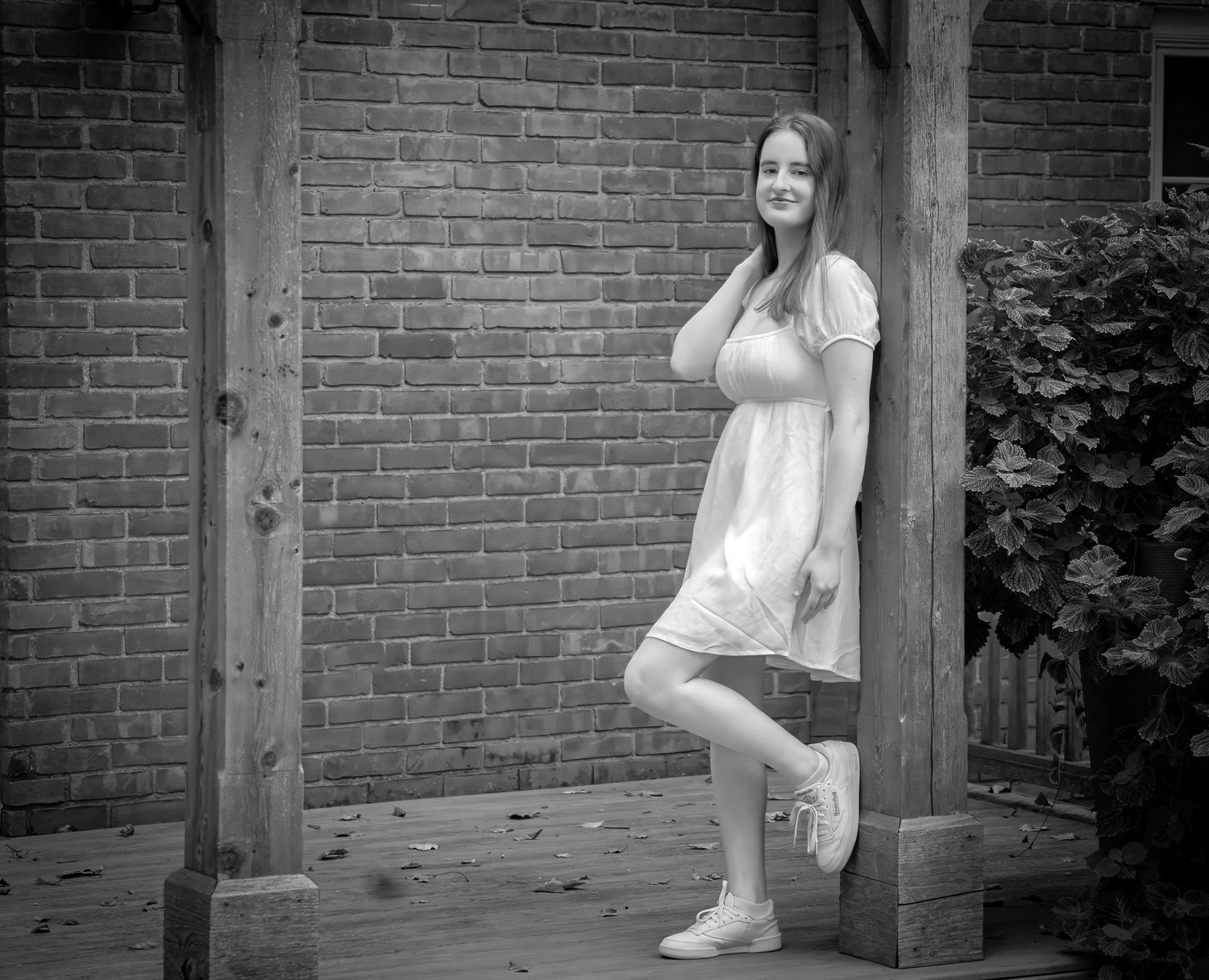 Black and white portrait of a teenage girl in white dress by brick wall.