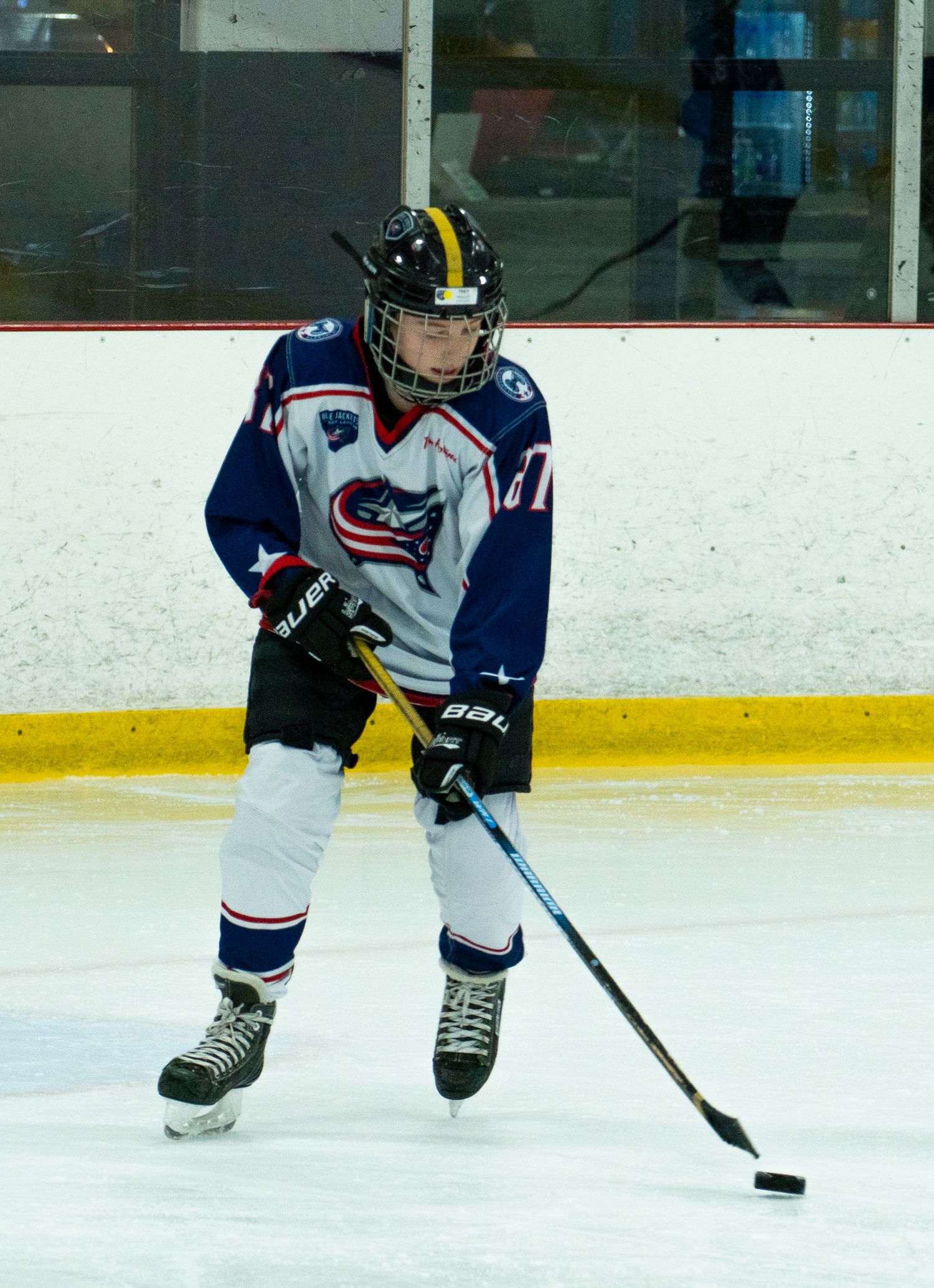 A young ice hockey player in blue and white uniform skating with a puck during a game.