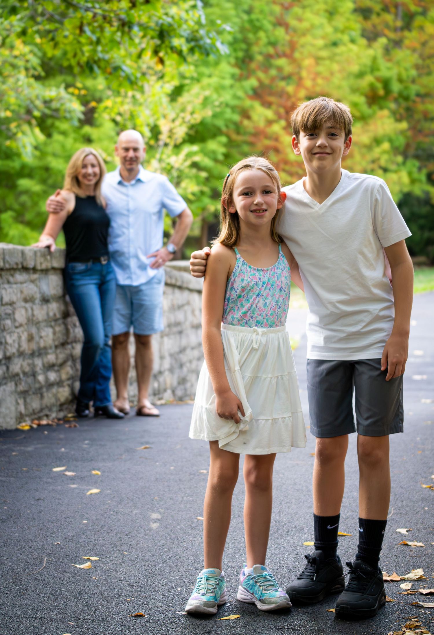 Family of four posing on a tree-lined path, two children in front smiling at camera.