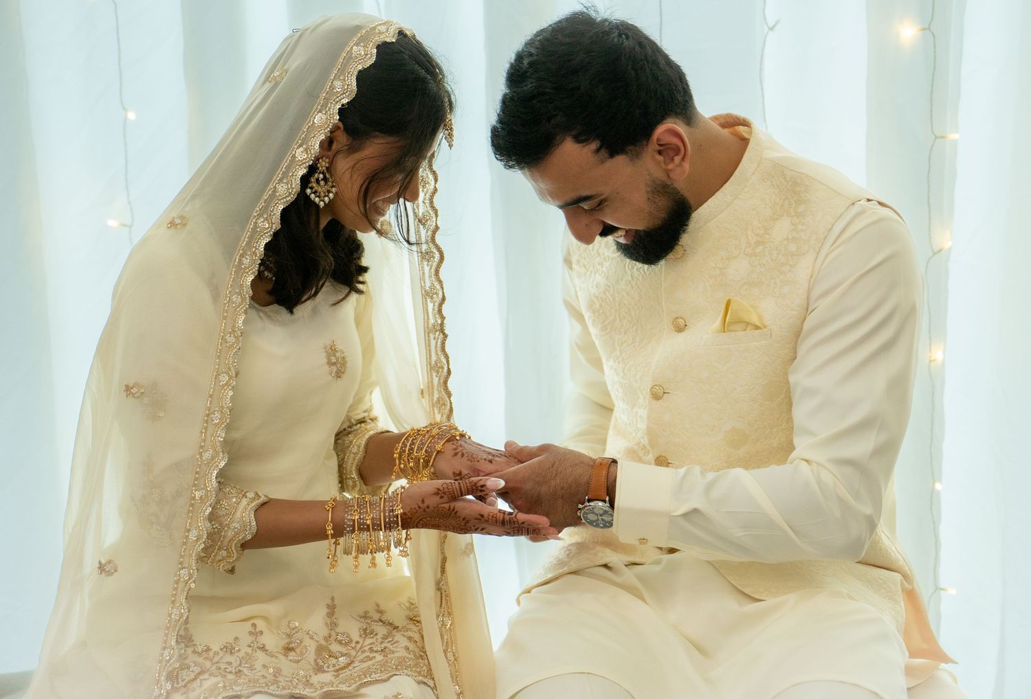 South Asian couple in white wedding attire during a ring exchange ceremony.