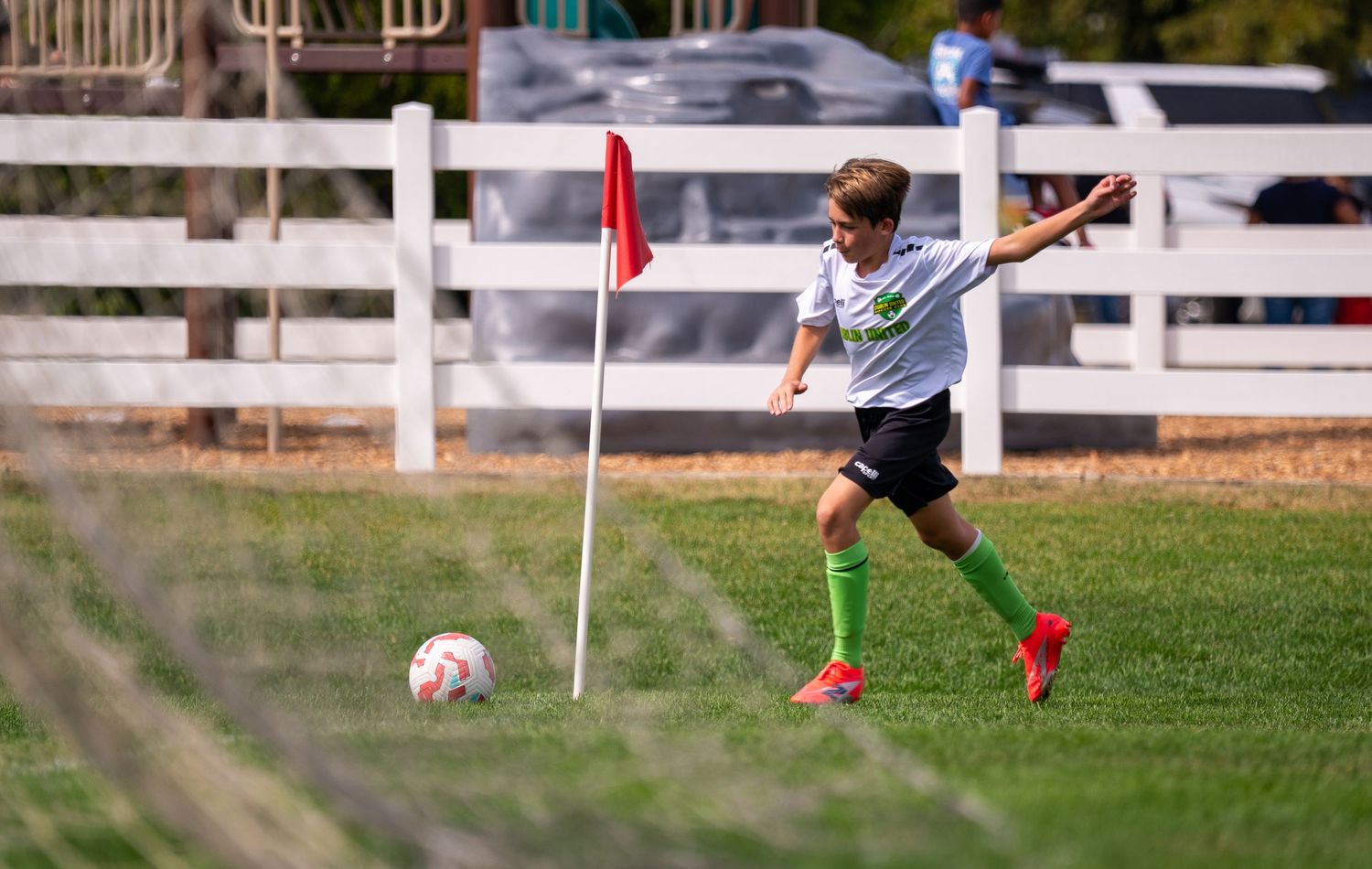 Young soccer player kicking the ball near a corner flag during a youth soccer match outdoors.