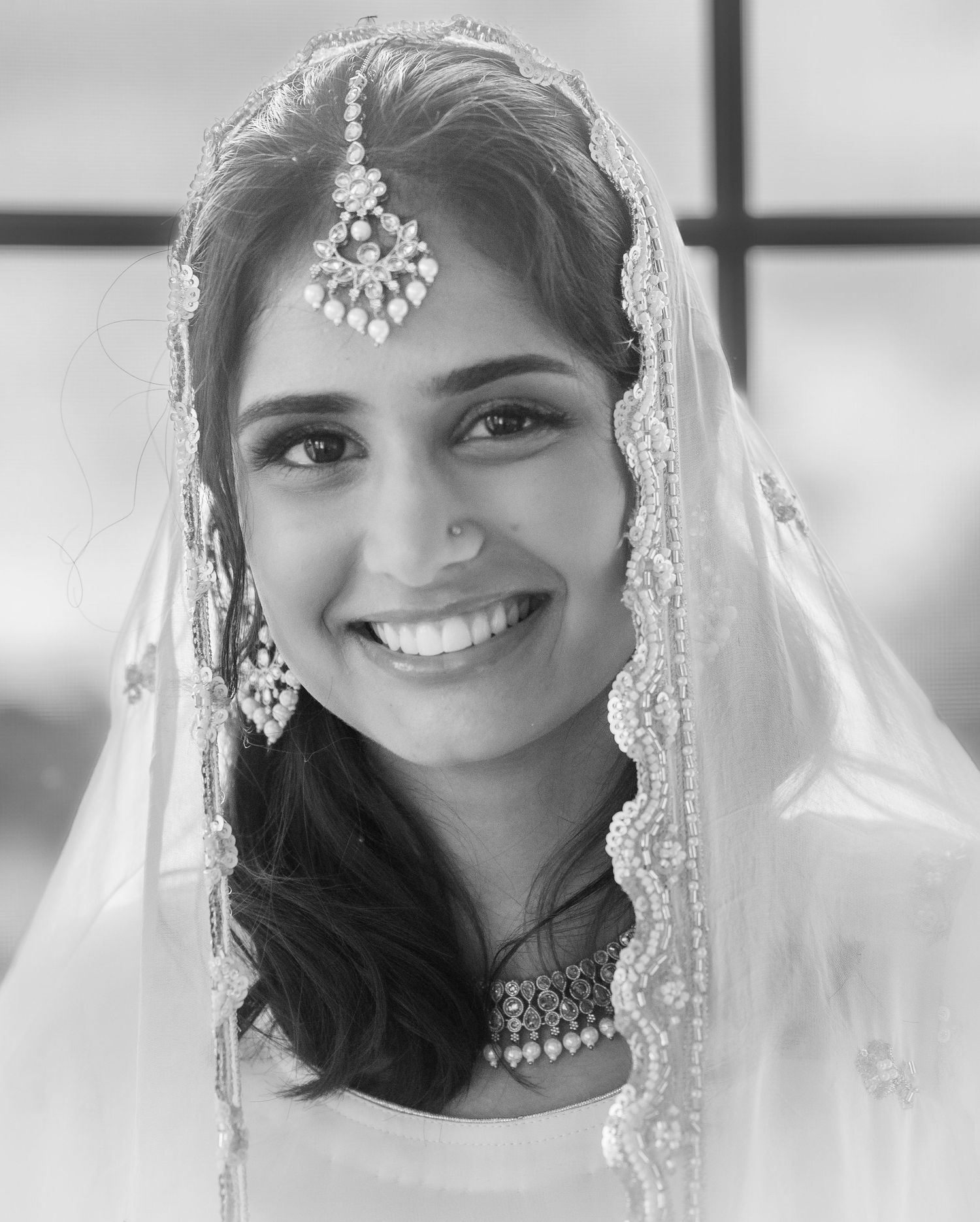 Black and white portrait of smiling South Asian bride wearing traditional maang tikka and wedding veil.