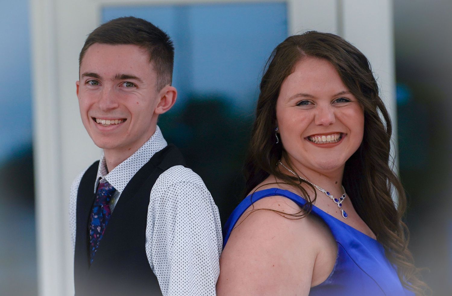 A young man in a suit and a woman in a blue gown smile together at a formal prom event.