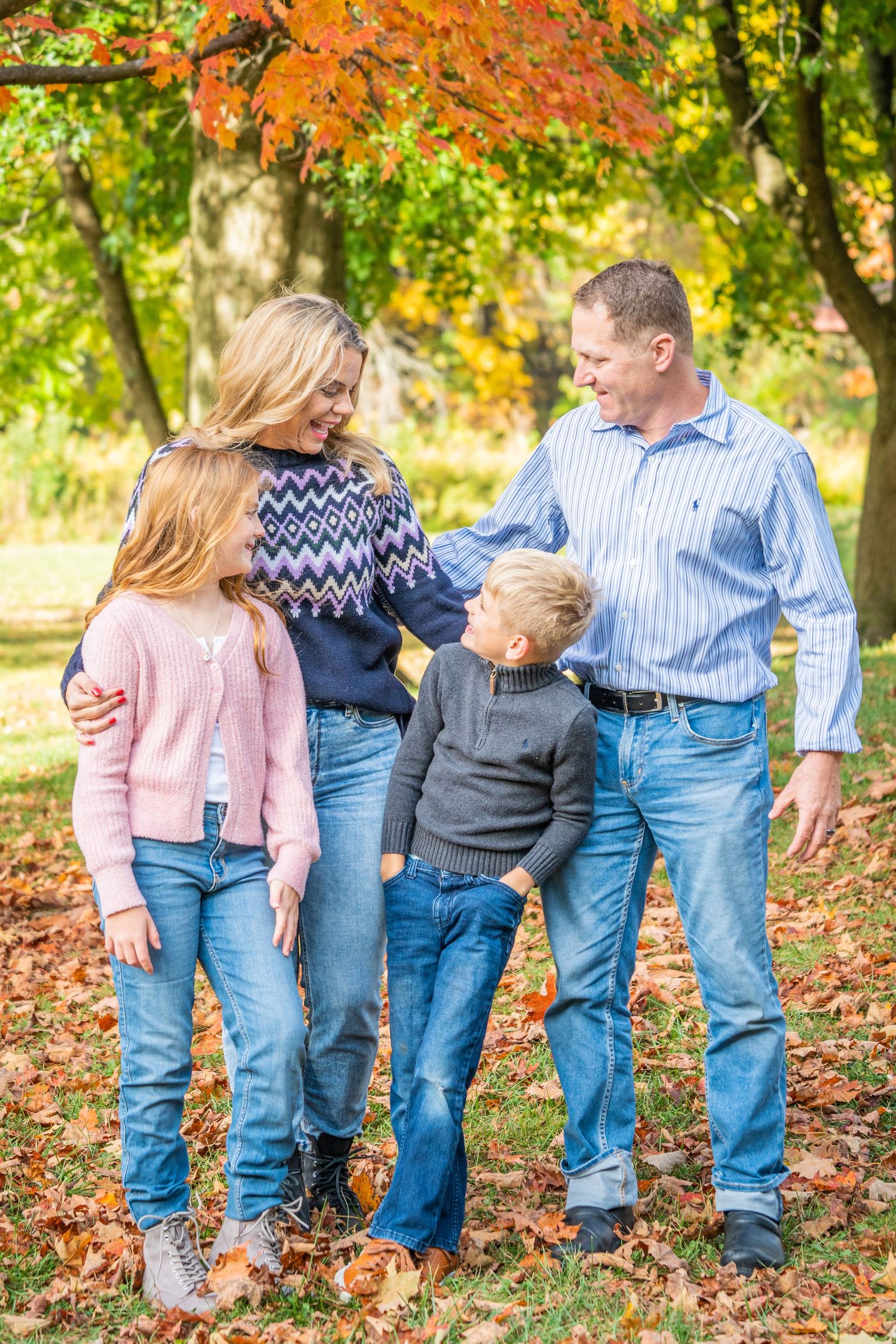 Happy family of four standing in colorful autumn leaves park, smiling and enjoying fall season together.