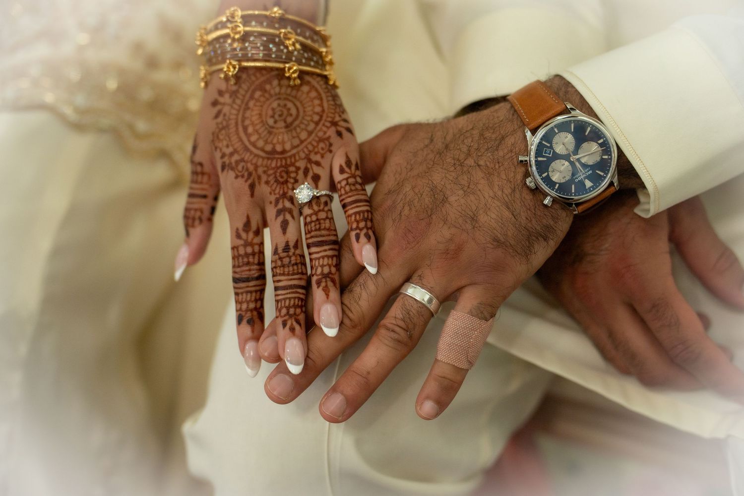 Close-up of bride and groom's hands showing henna, wedding rings, and luxury watch after Nikah.