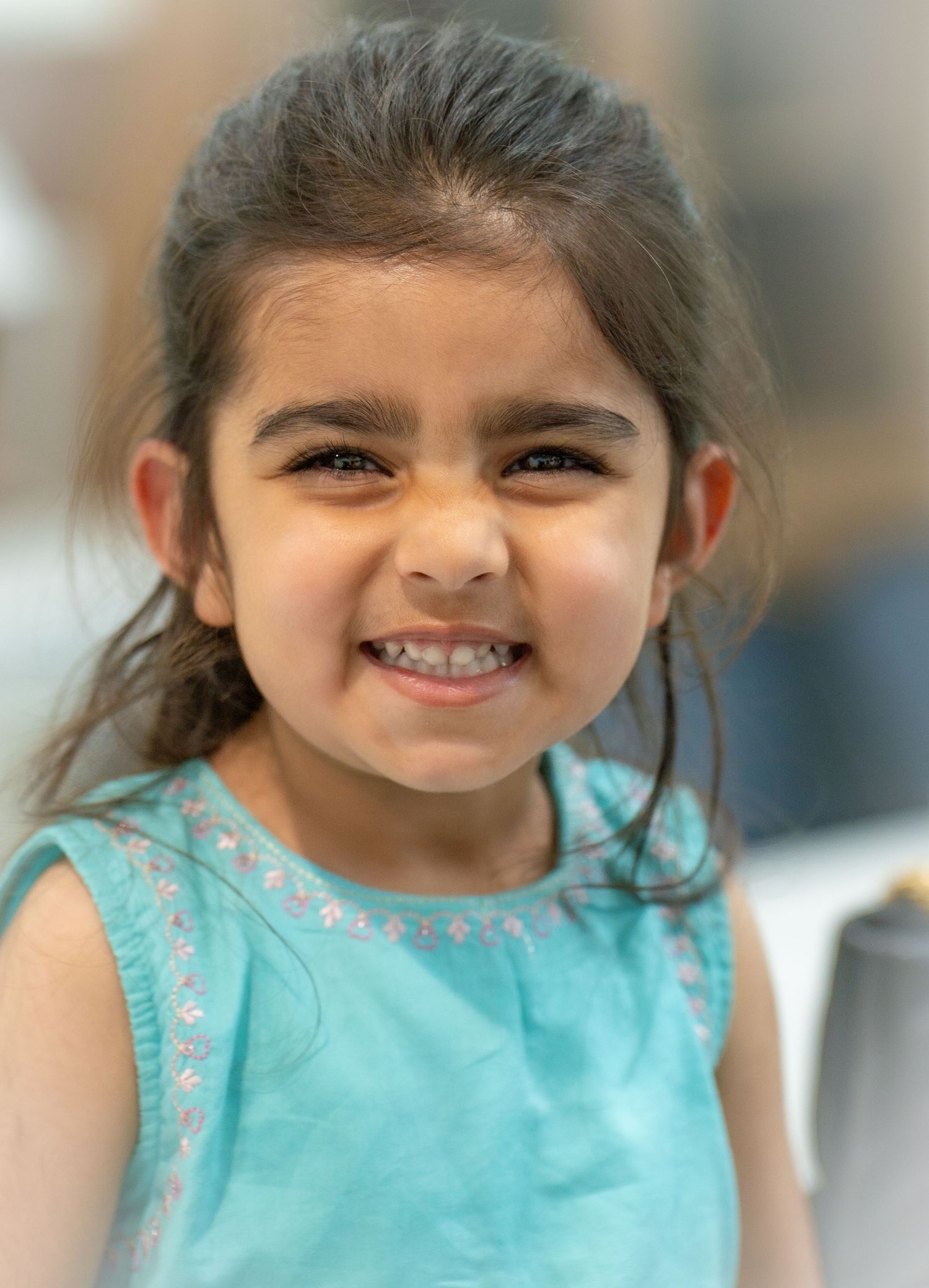 Adorable young girl in teal dress grinning with bright expressive eyes.