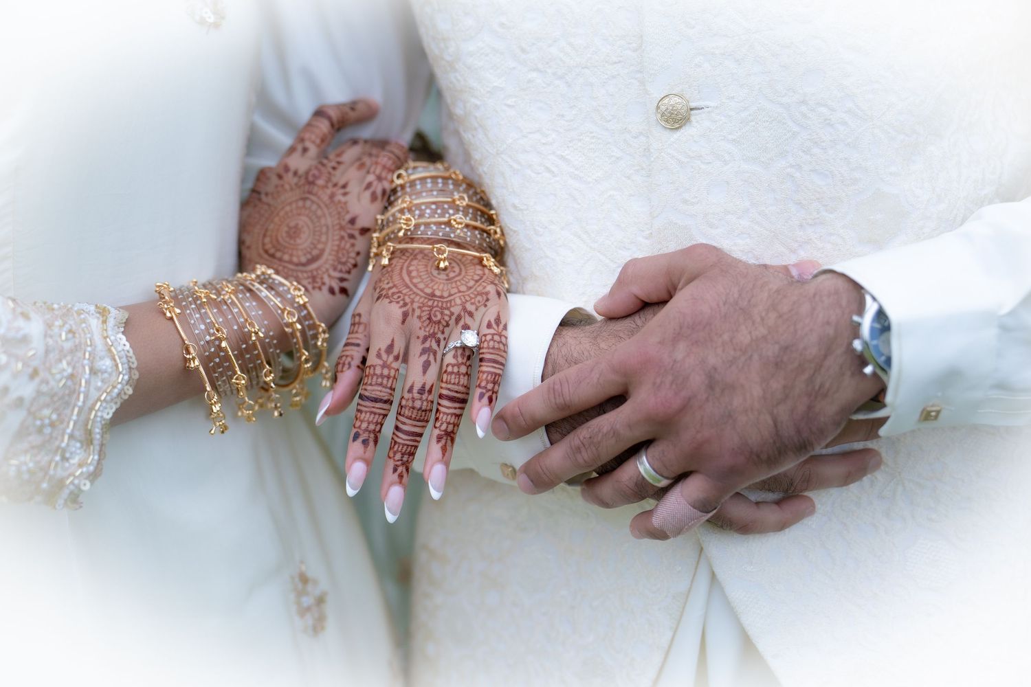 Close-up of bride's hands adorned with intricate mehndi henna and gold bangles on wedding day.
