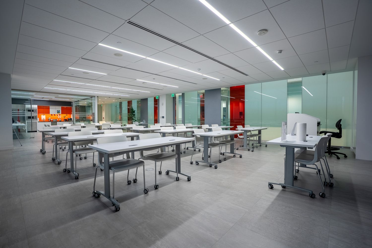 Modern empty classroom with white desks on wheels, ergonomic chairs, bright LED lighting, and glass partition walls.