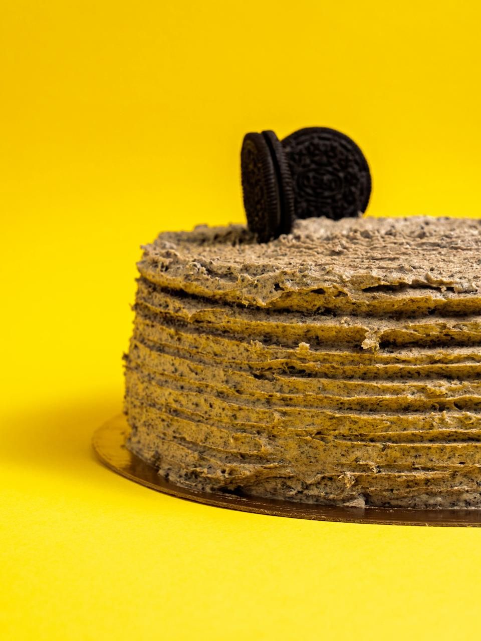Oreo cookies and cream layered cake with textured frosting on a gold base against a bright yellow background.