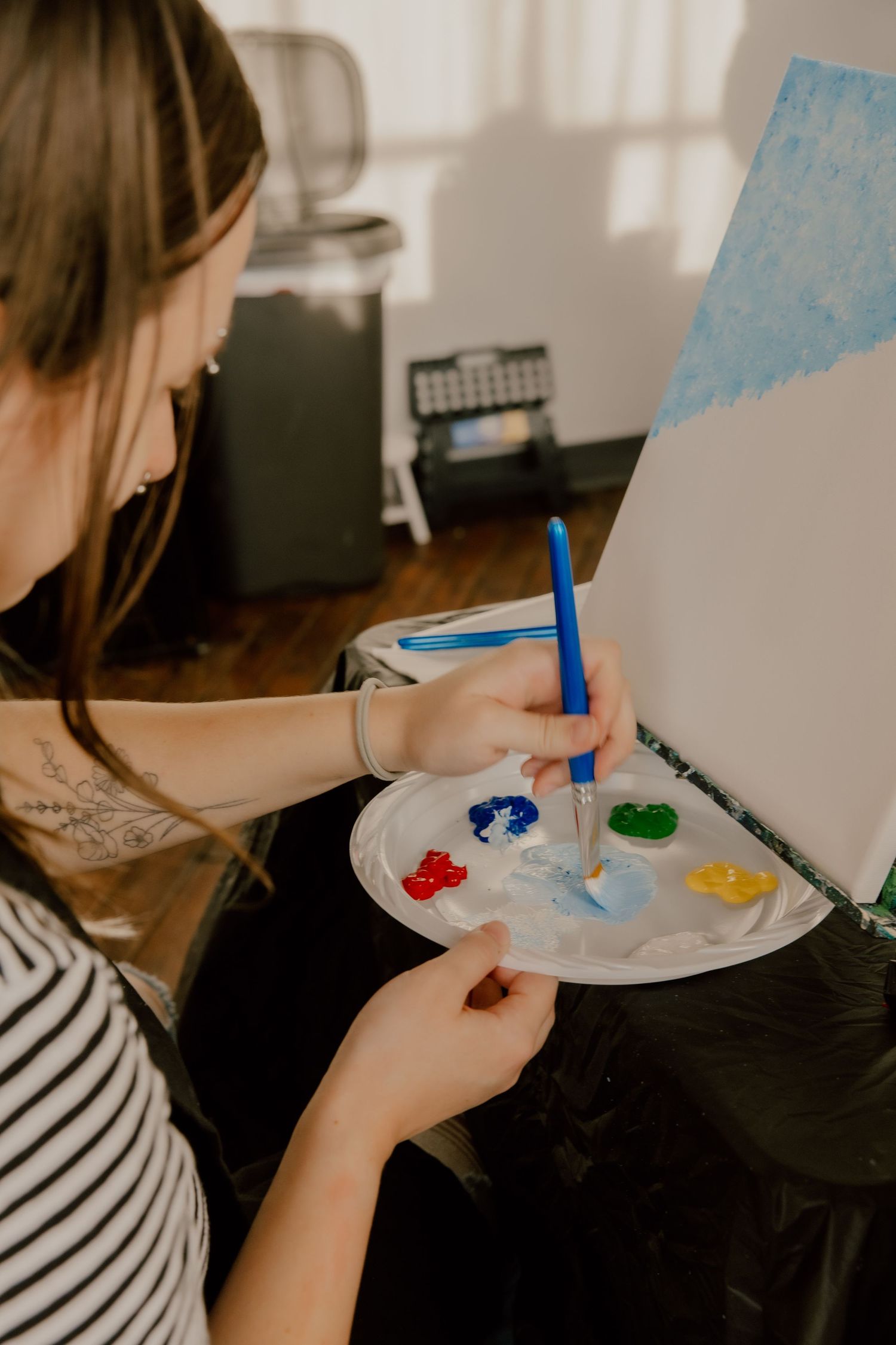 Young woman artist holding a paint palette with colorful paints, using a blue brush to paint on canvas.