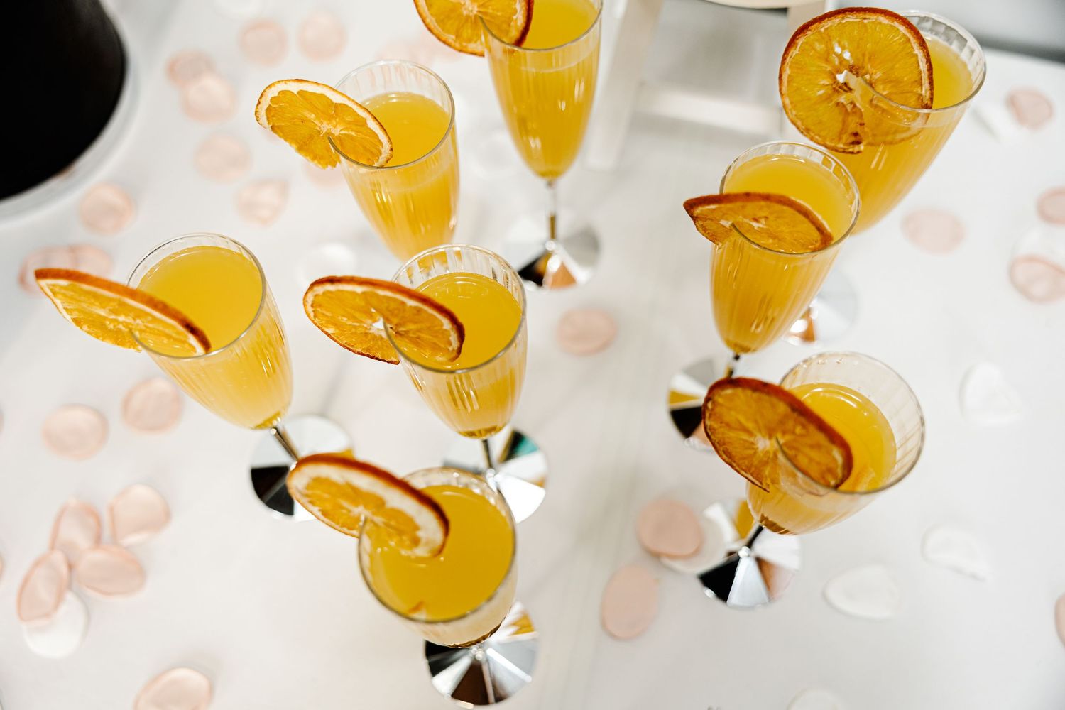 Elegant champagne flutes filled with orange juice and garnished with citrus slices on a white table.
