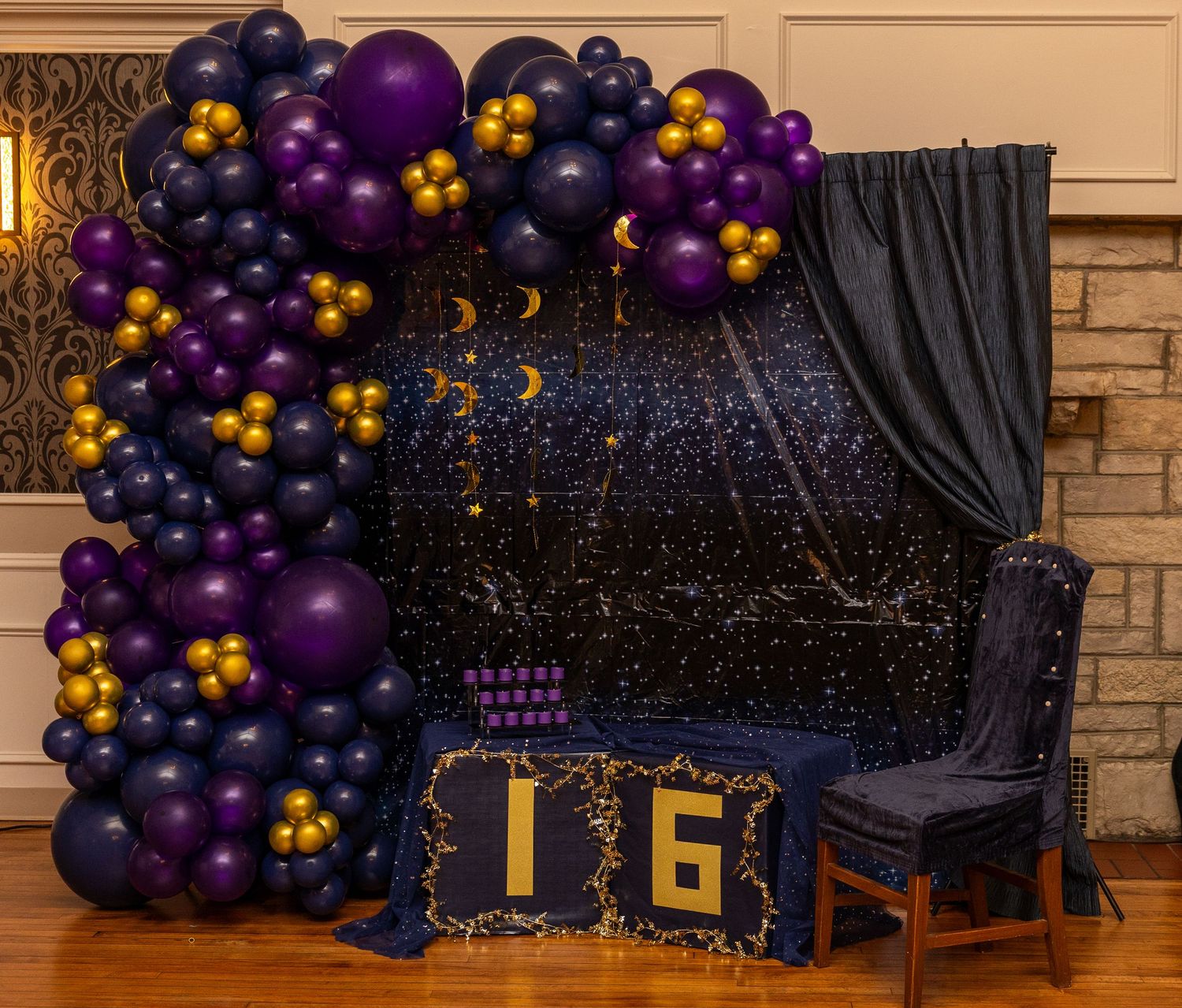 Purple, black, and gold balloon garland arch decorates a Sweet 16 birthday party backdrop with celestial theme.