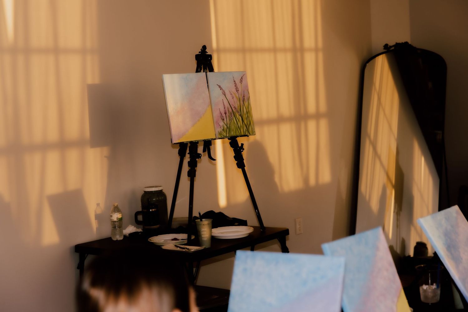 A painting on a wooden easel in a warmly lit art studio with soft sunlight casting shadows on the wall.