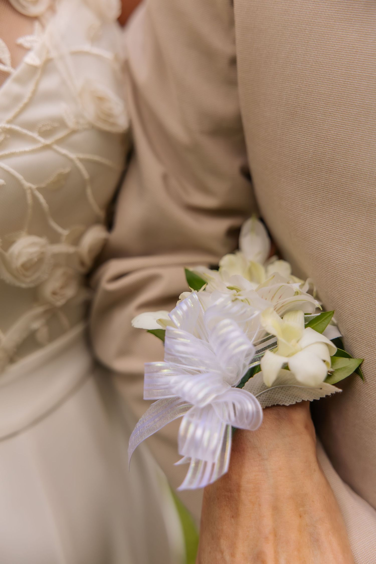Close-up of a white floral wrist corsage with satin ribbon bow on a wedding guest's wrist.