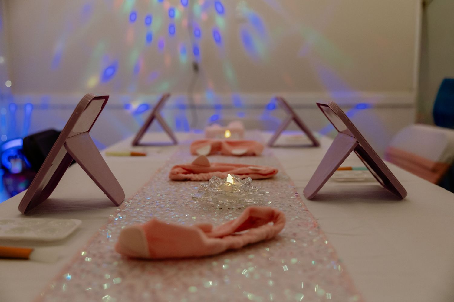 Elegant party table with glittery runner, pink napkins, mirrors, and colorful bokeh lights in the background.