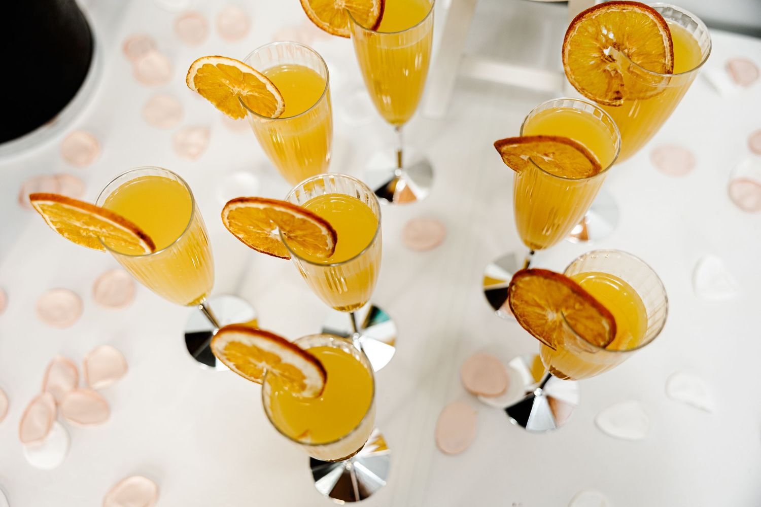 Elegant champagne flutes filled with orange juice and garnished with citrus slices, arranged on a white surface.