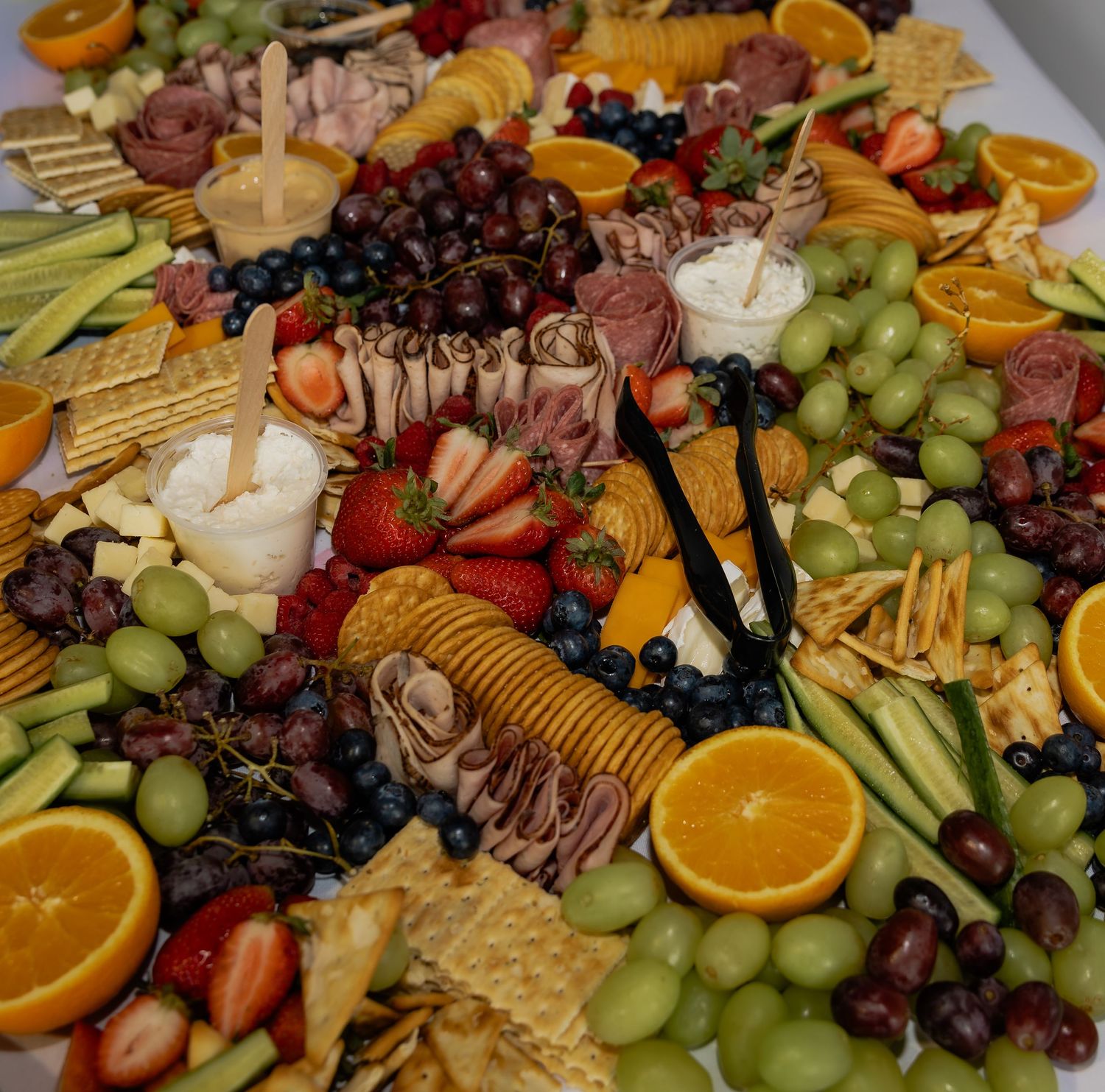 Elegant charcuterie board with grapes, strawberries, oranges, crackers, cured meats, cheese, and blueberries.