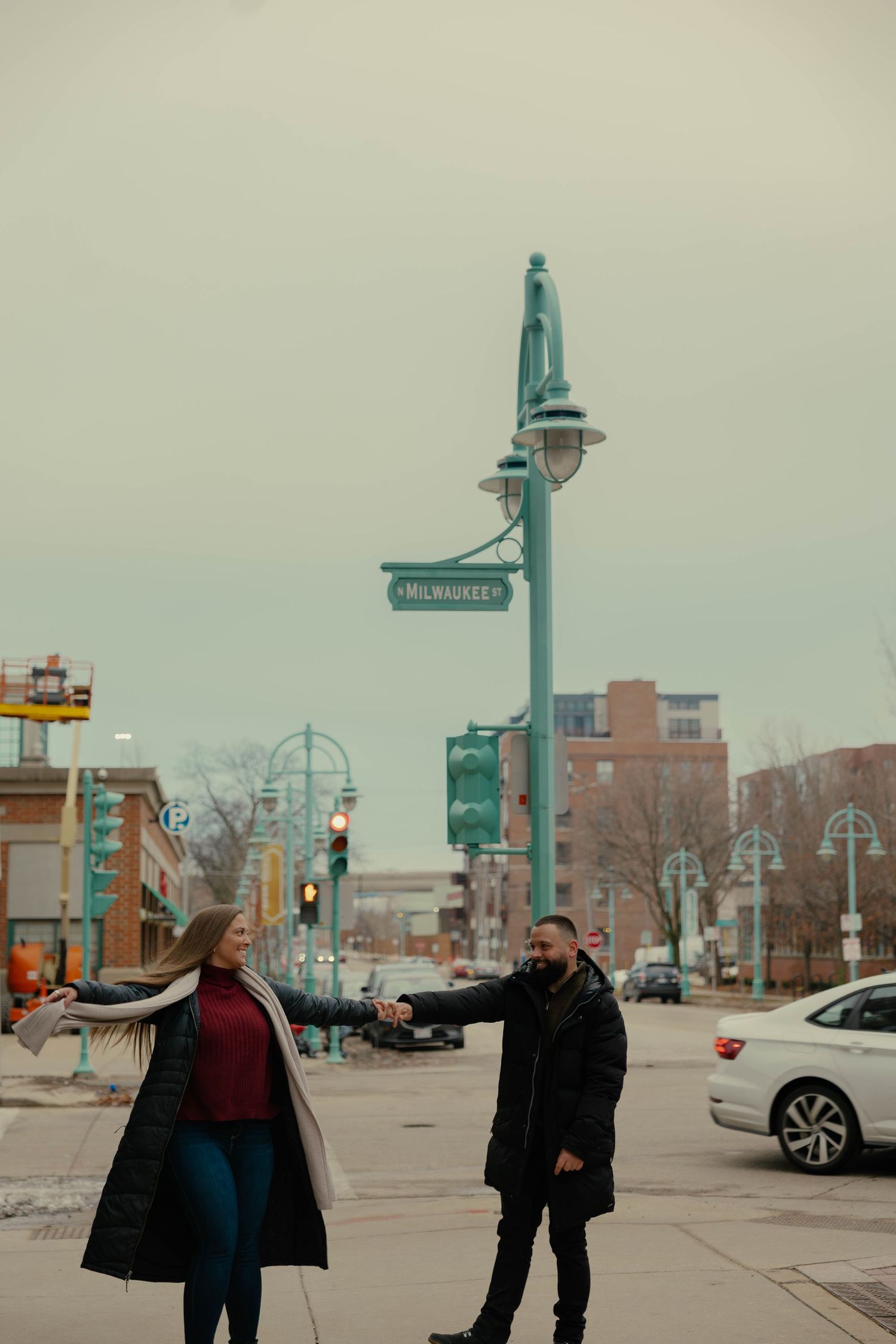 Couple holding hands at Milwaukee street intersection on a cloudy day in an urban setting.