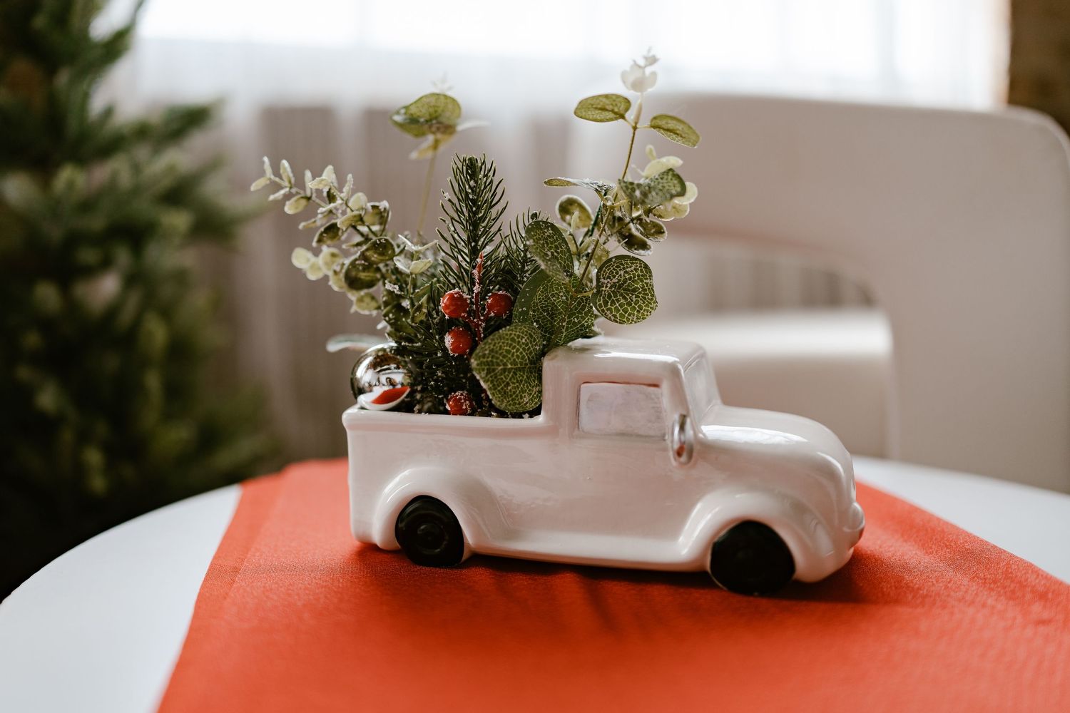 White ceramic truck planter with festive greenery and berries on a red mat, perfect for holiday home decor.