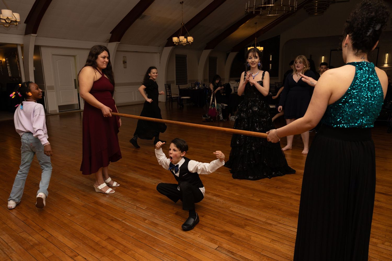 People playing limbo at a formal dance event on a wooden floor in an elegant ballroom venue.