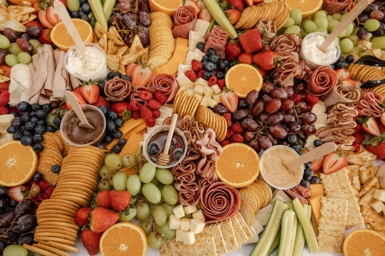 Colorful charcuterie board with fresh fruits, cheeses, crackers, meats, grapes, strawberries, and oranges arranged beautifully.