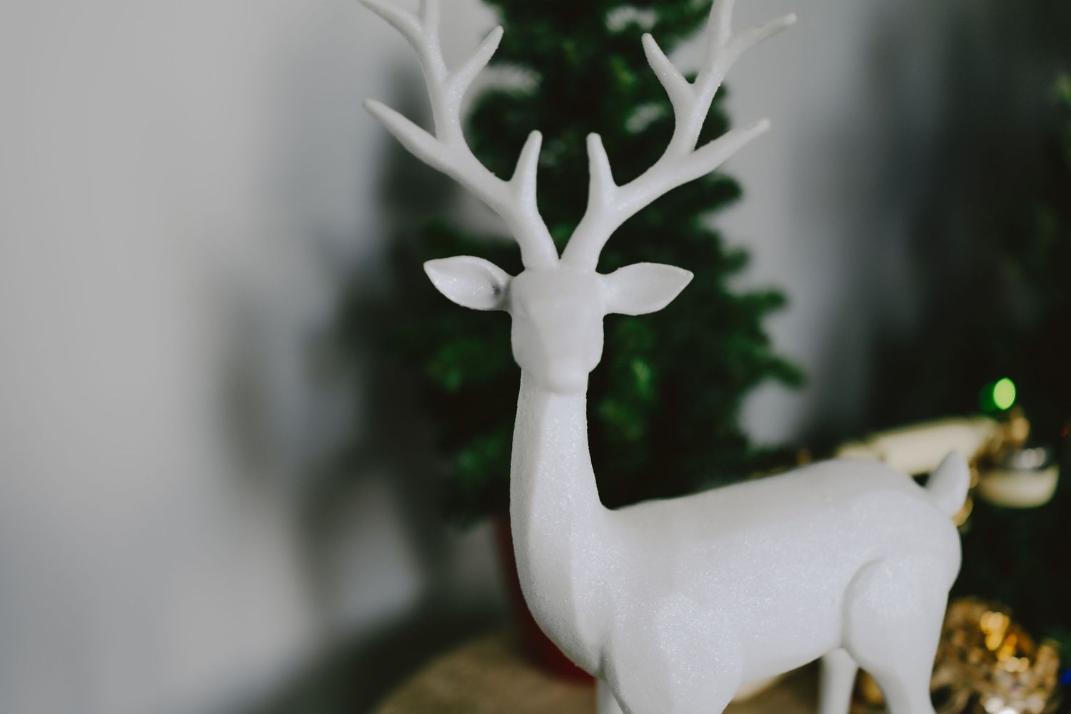 White ceramic reindeer figurine with antlers displayed in front of a blurred Christmas tree holiday decoration.