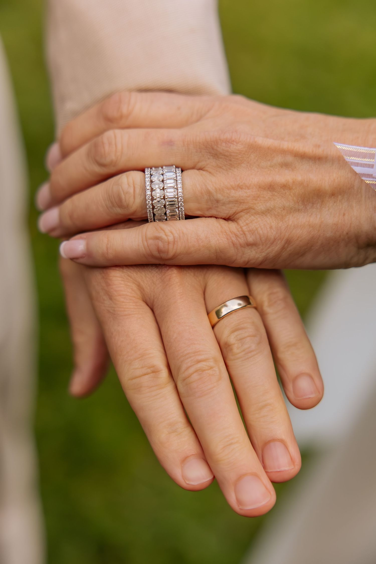 Two hands with wedding rings, one with a diamond band and one with a gold band, resting together on a green background.