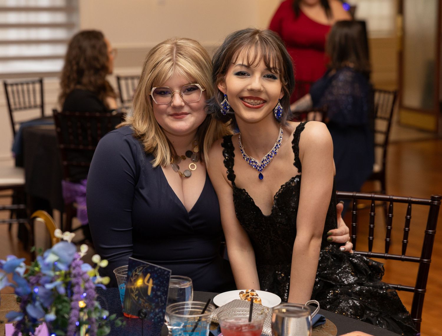 Two women in elegant evening gowns smile together at a formal gala dinner event.