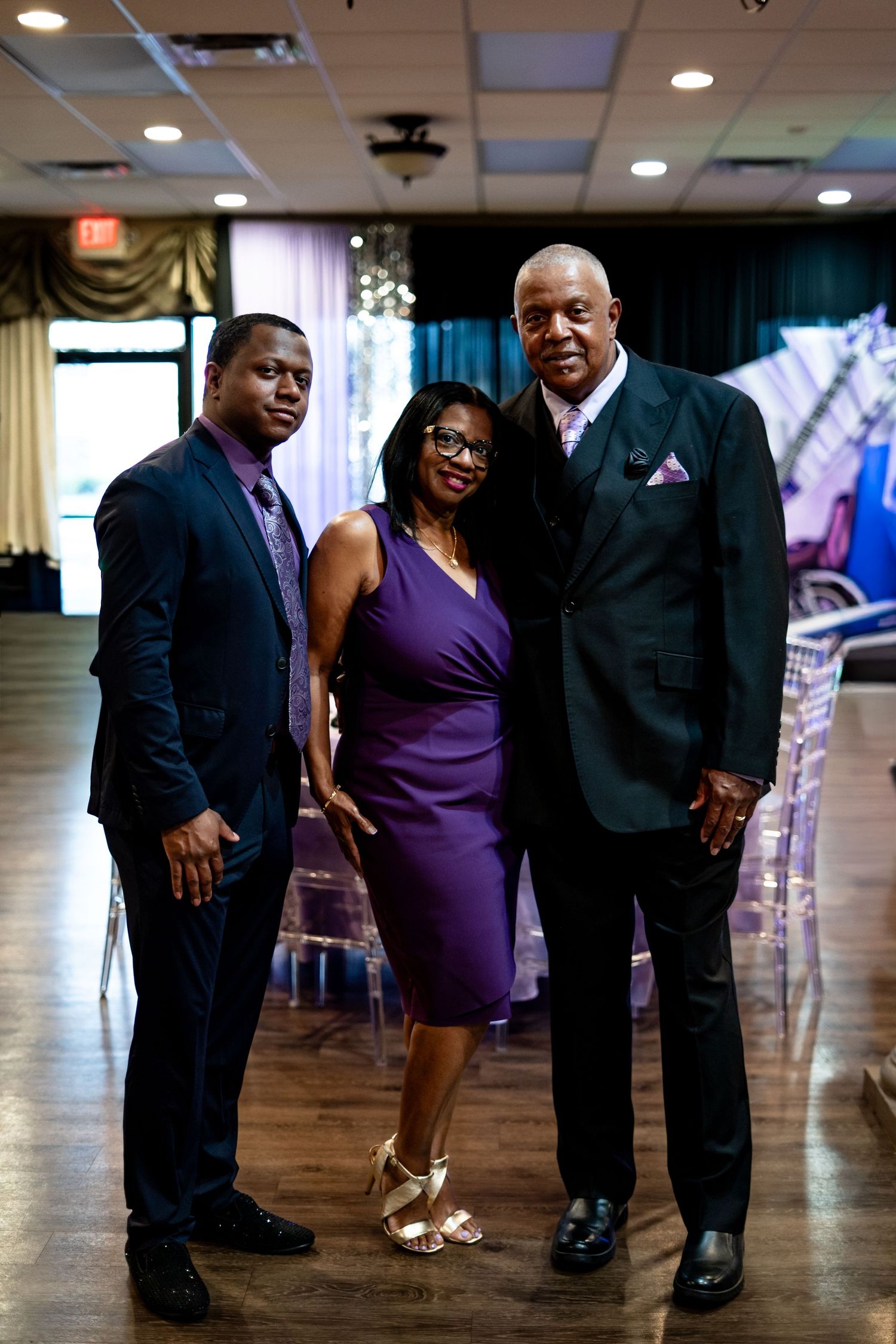 Three elegantly dressed guests posing together at a formal birthday celebration in a decorated banquet hall.