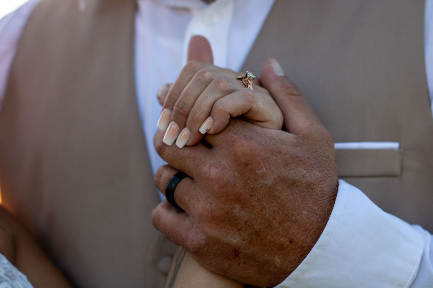 Close-up of bride and groom holding hands showing wedding rings.