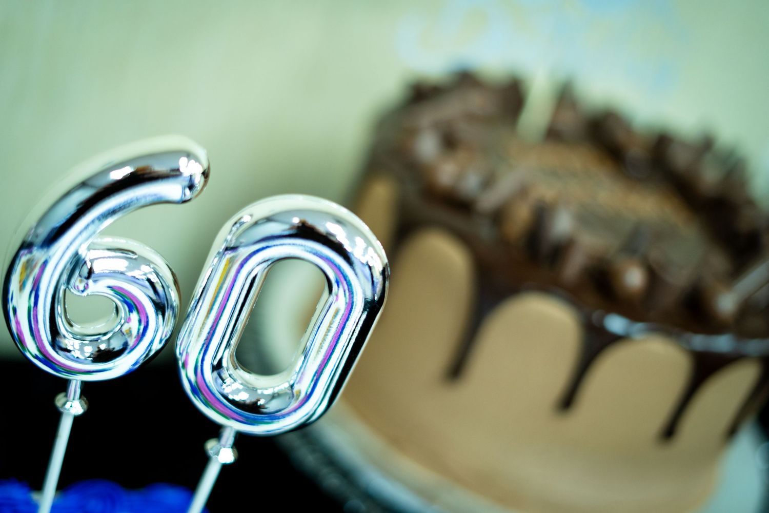 Silver number 60 candles displayed in front of a chocolate drip birthday cake for a milestone celebration.