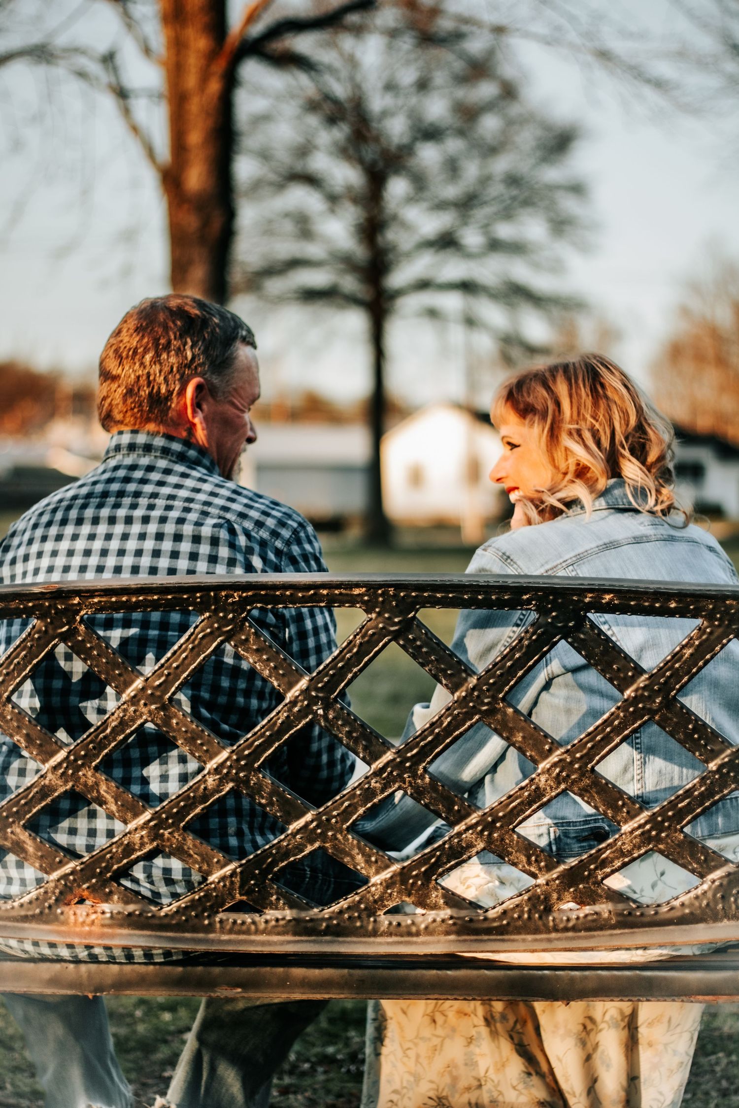 Couple sitting together on an ornate metal park bench at golden hour, sharing an intimate conversation outdoors.