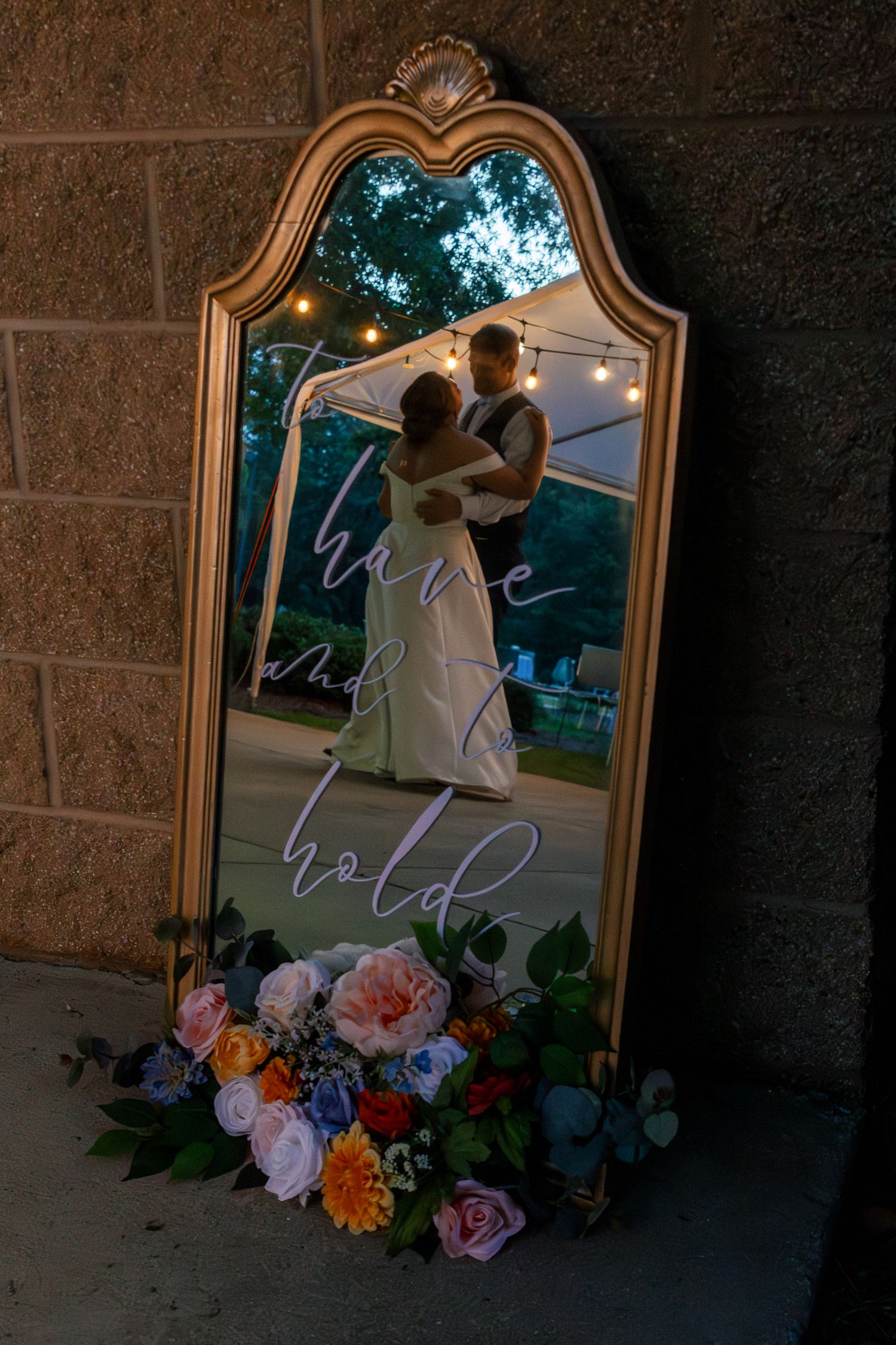 Ornate gold mirror decorated with pink and purple flowers reflects an ethereal bridal scene at dusk.