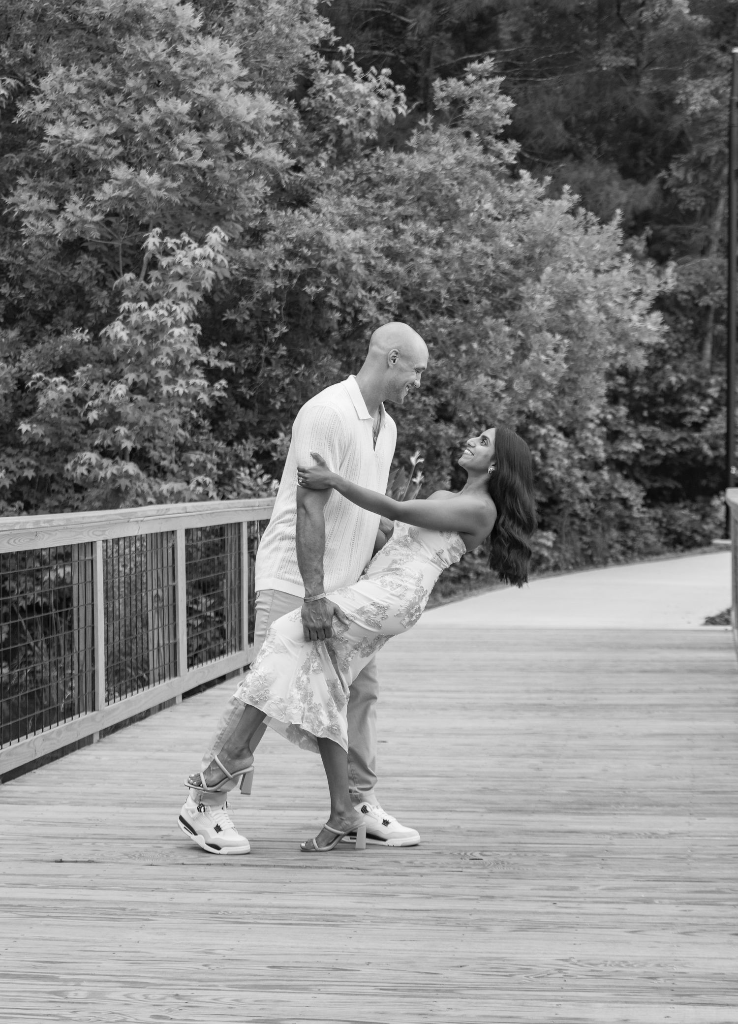 Black and white photo of couple dancing and dipping on a scenic wooden bridge outdoors.