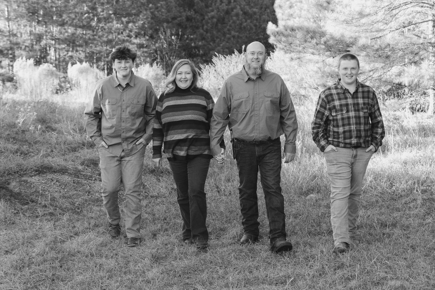 A family of four walks together through a grassy field in a classic black and white portrait.