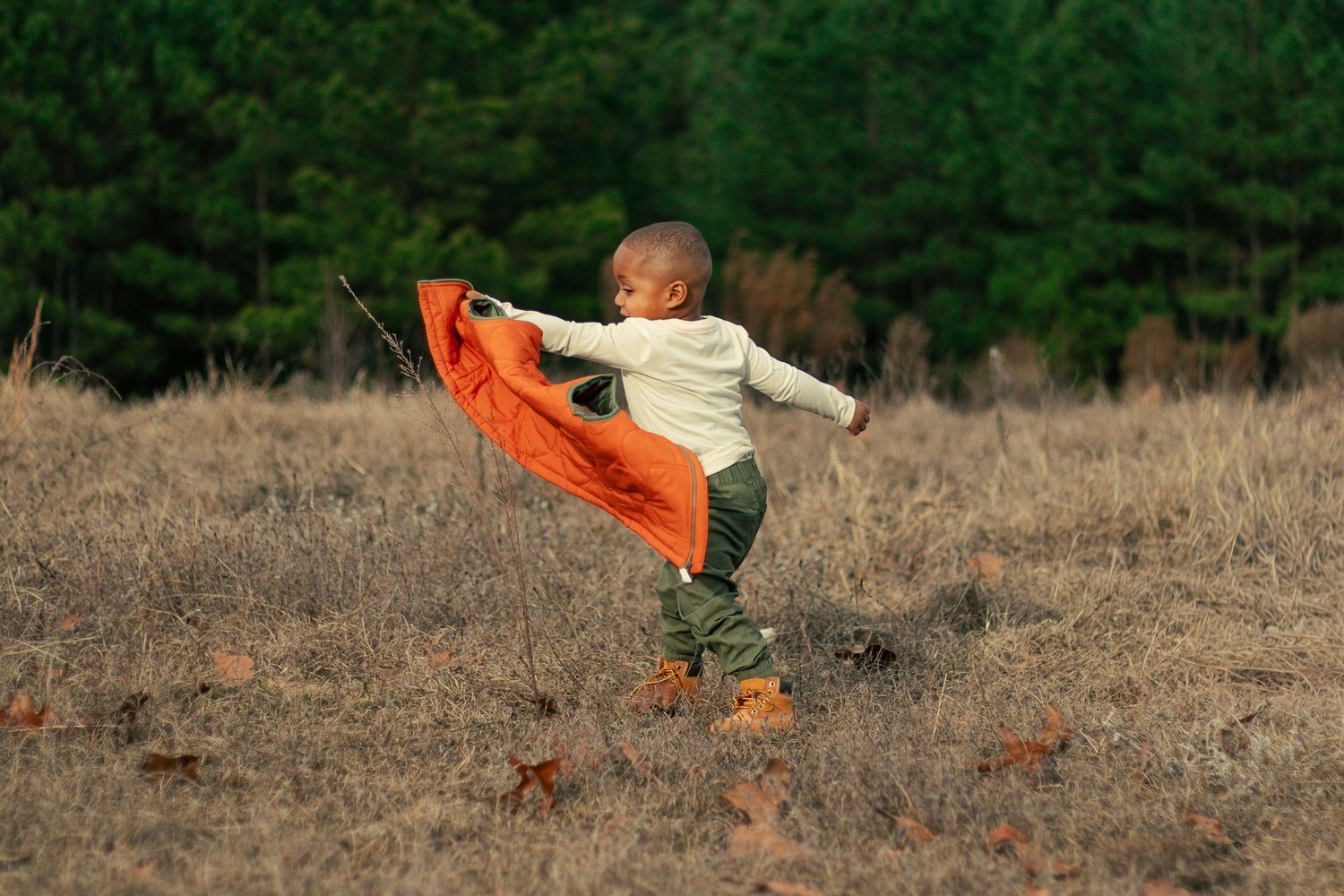 A bright orange scarf flows gracefully through the air against a natural outdoor backdrop with dry grass and trees.
