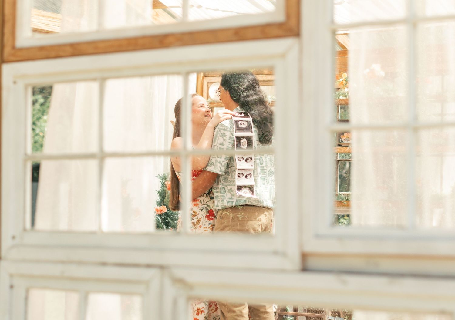 Two women reflected in a vintage white-framed window, sharing an intimate moment in a warmly decorated room.