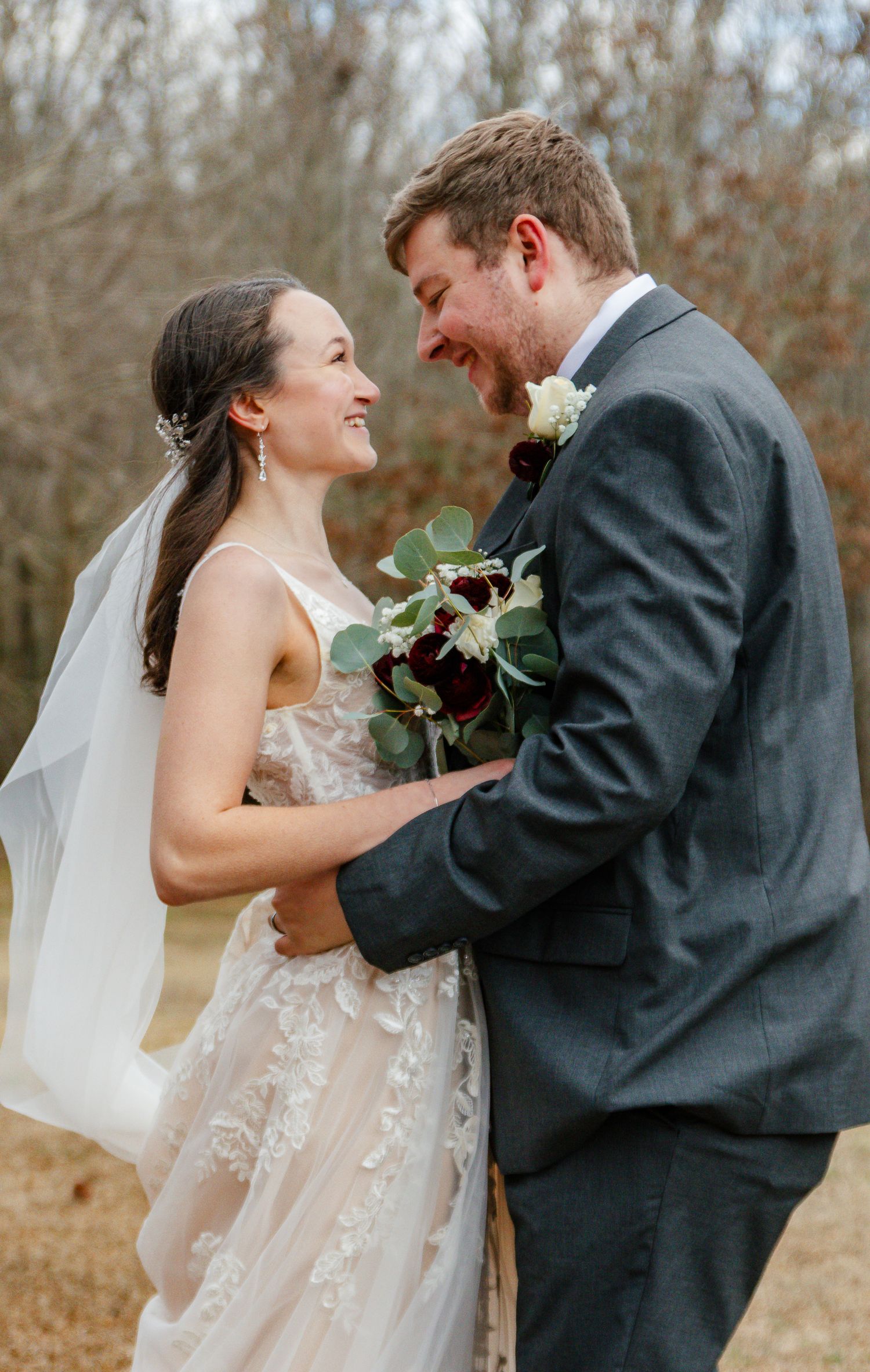 A joyful couple shares a candid moment together outdoors during their wedding ceremony, with a bouquet of eucalyptus.