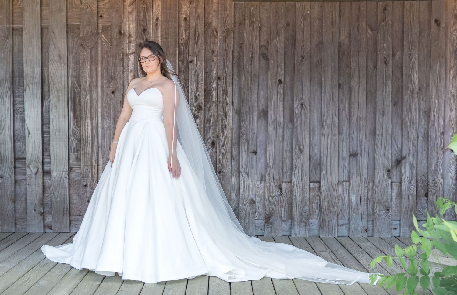 Bride in a white ball gown and long veil posing against a rustic wooden barn wall during a South Carolina bridal portrait session.
