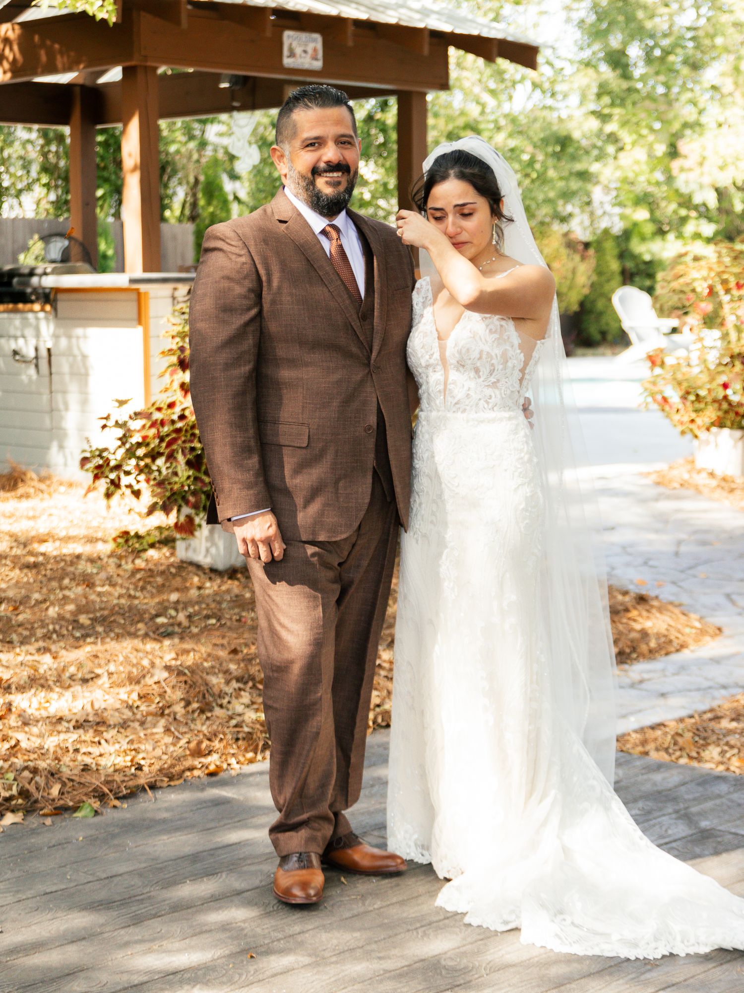 A couple in wedding attire shares a joyful moment together under a wooden gazebo during their outdoor celebration.