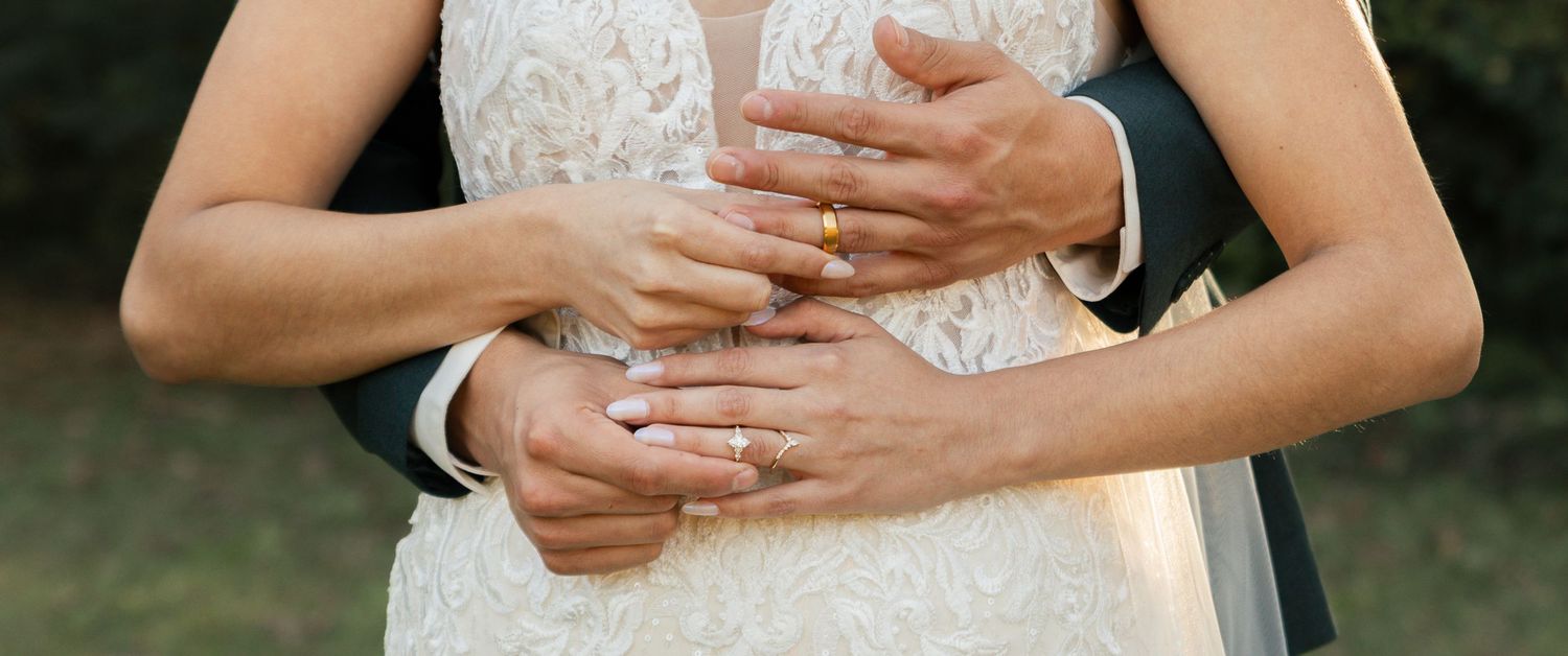 Close-up view of hands gently clasped together against a white lace dress in an outdoor setting. Lexington Wedding Photographer