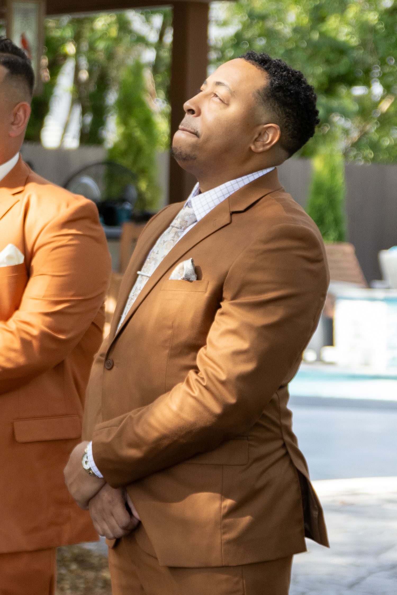 A person in a brown suit jacket poses expressively in a series of four connected photos outdoors.