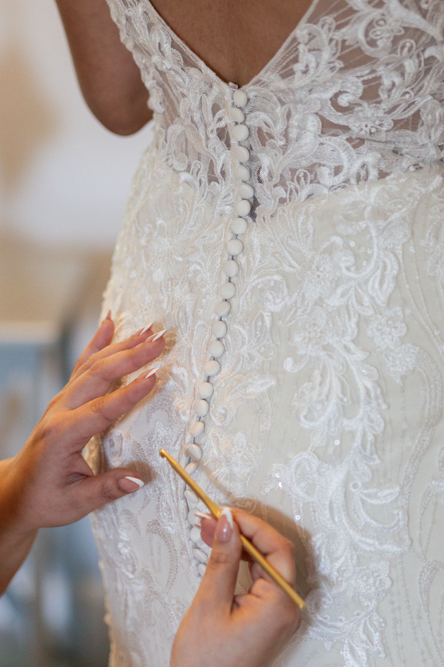 Close-up of hands making detailed adjustments to delicate white lace beadwork on a wedding dress bodice.