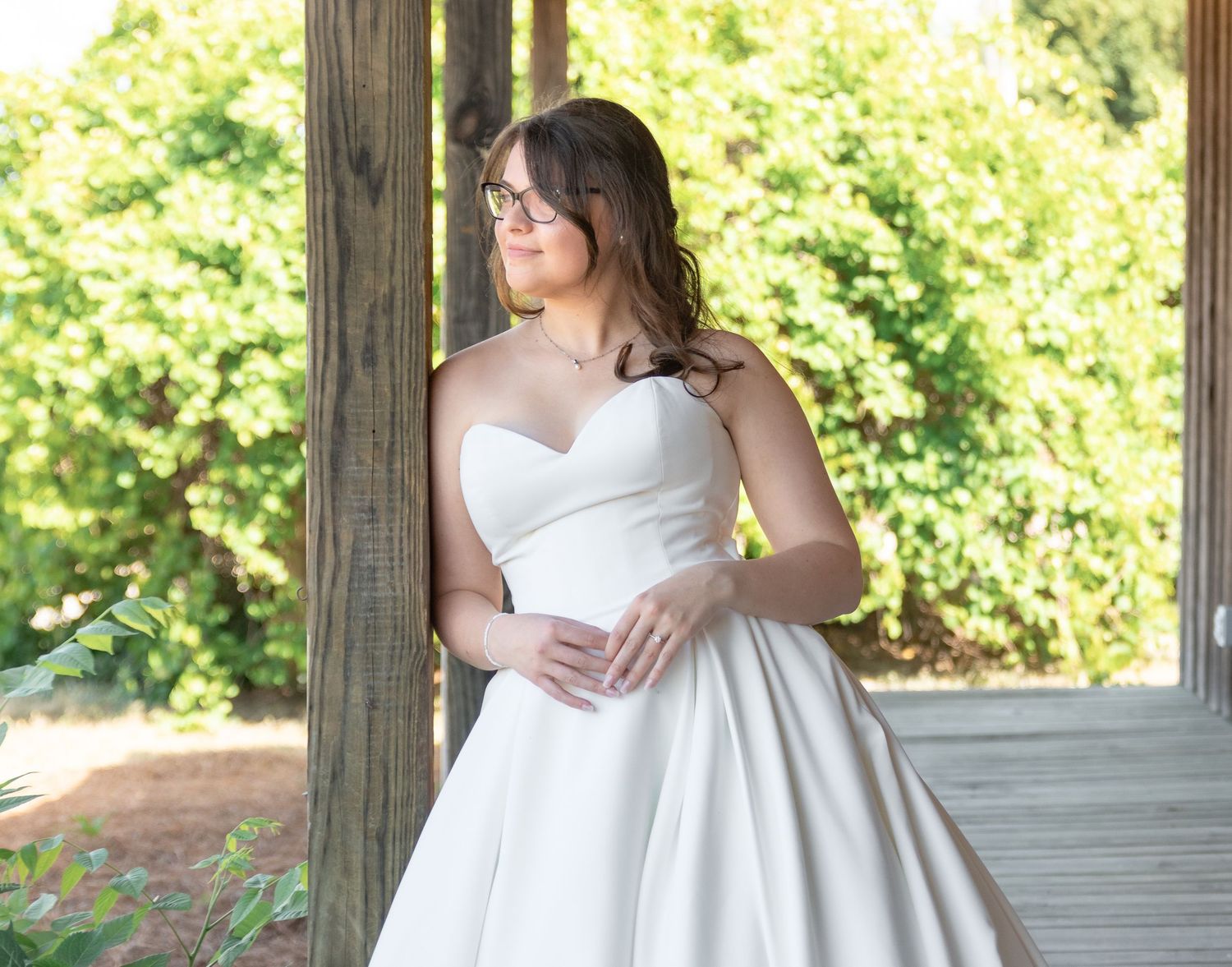 Bride in a strapless white ball gown posing outdoors near a wooden pergola during a South Carolina bridal portrait session.